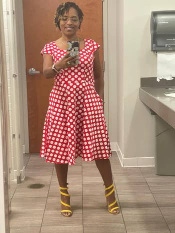 Reviewer in a red polka dot dress and yellow strappy heels posing for a mirror selfie