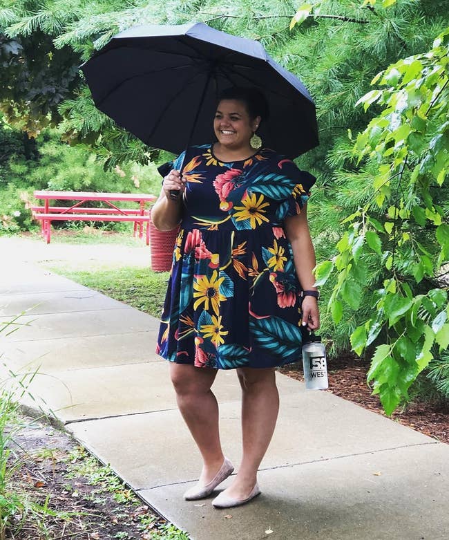 reviewer in a navy blue floral dress with ruffled sleeves holding umbrella