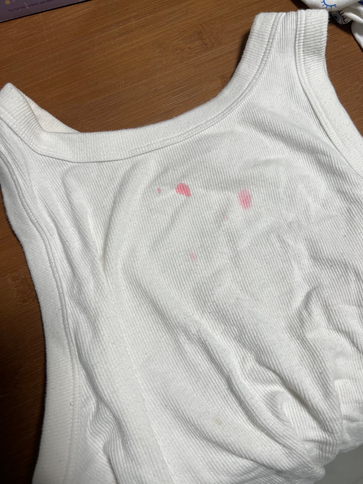 White tank top with faint pink stains on the front, placed on a wooden surface