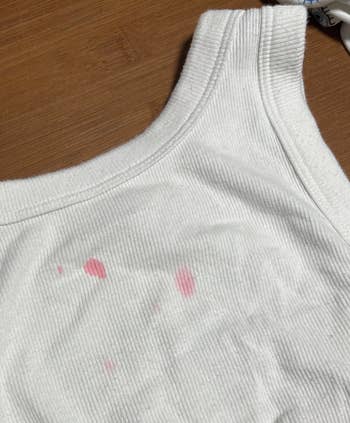 White tank top with faint pink stains on the front, placed on a wooden surface