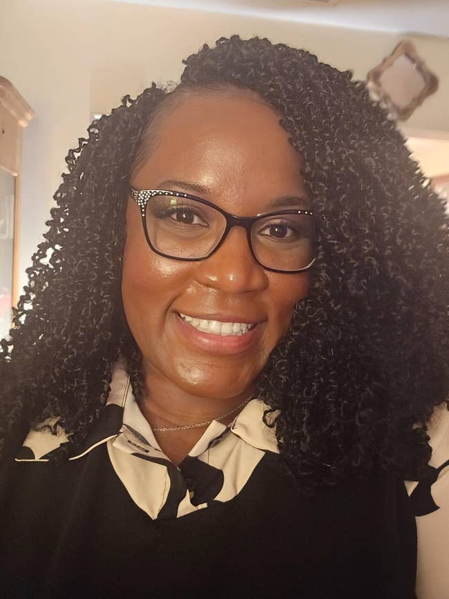 A idiosyncratic   with curly hair, wearing glasses and a stylish collared top, smiles astatine  the camera