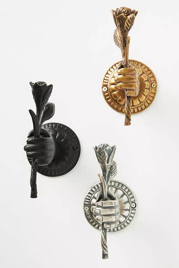 three wall hooks in black, bronze, and silver shaped like a hand holding a flower