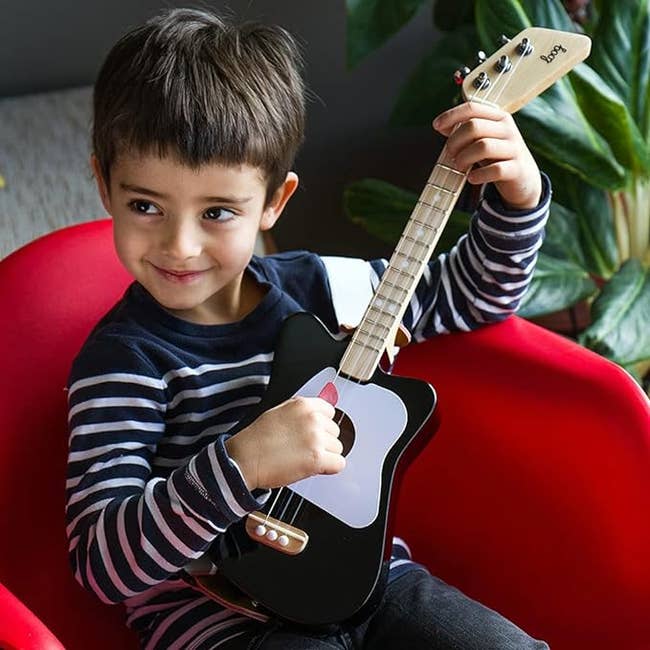 Child model playing a black, three-string guitar