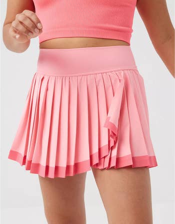 model wearing a pleated tennis skirt and pink crop top, midsection view