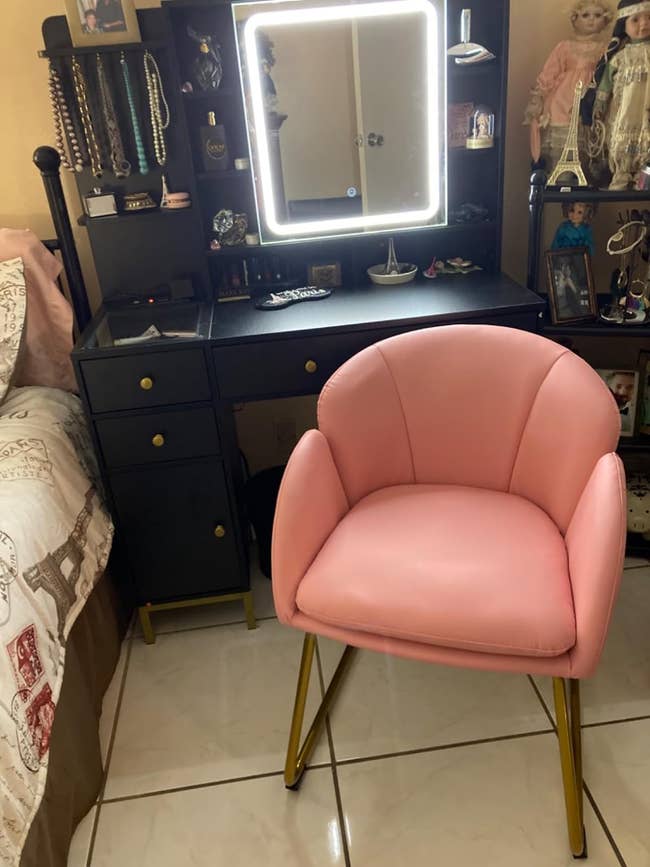 Pink chair in front of a vanity with a mirror and black drawers
