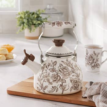 Vintage-style floral beverage  kettle with ornate grip  connected  woody  board, matching mug nearby. Perfect for adding elegance to room  decor