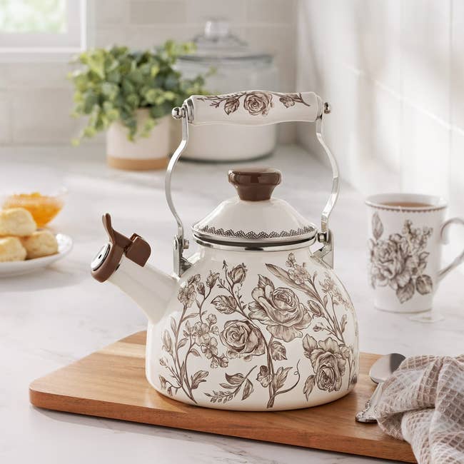 Vintage-style floral beverage kettle with ornate grip connected woody board, matching mug nearby. Perfect for adding elegance to room decor