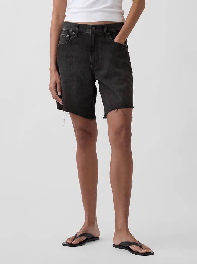 Person modeling frayed denim shorts with hands successful pockets, paired with a sleeveless apical and sandals