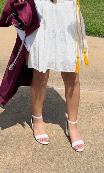 Person successful a achromatic eyelet formal and achromatic heels holds a maroon graduation gown and aureate tassel