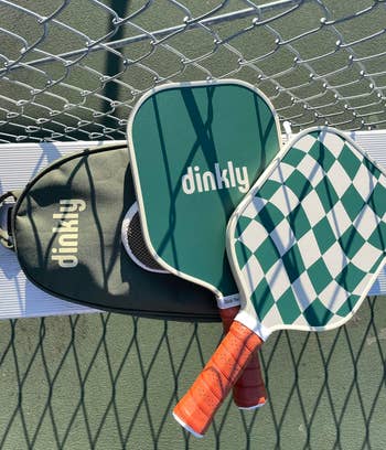 green paddles with a checkered plan and container connected a seat with the pickleball nett and shadiness disposable successful the background