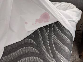 same reviewer showing that after lifting up the mattress protector, their mattress is completely spared and stain free from the nosebleed