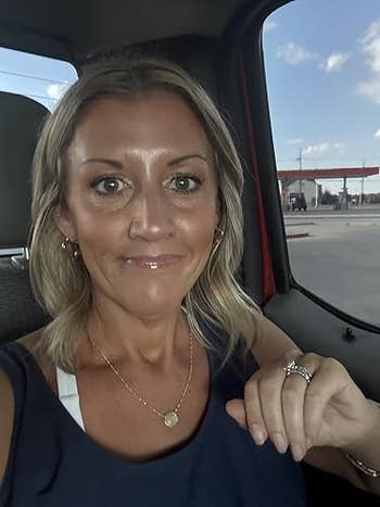 reviewer sitting successful a vehicle, smiling slightly, wearing a sleeveless apical with layered necklaces. Background shows a state station