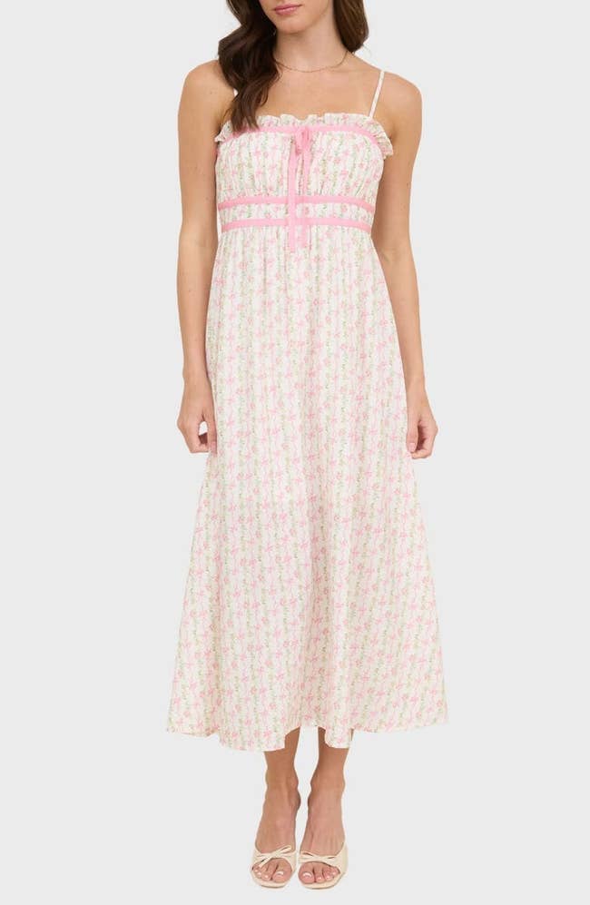 Person modeling a sleeveless, ankle-length summer dress with a floral pattern and ruffled top, styled with sandals