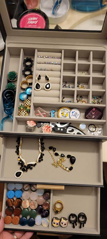 A jewelry organizer with an assortment of rings, earrings, necklaces, and pins. Includes beaded jewelry, novelty pins, and various types of rings