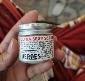 Hand holding Handmade Heroes' Ultra Sexy Scrub jar with product information, in a casual setting