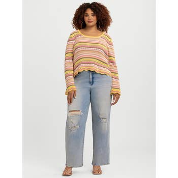 Person in a striped, long-sleeve sweater with distressed jeans and sandals, posing for a shopping article