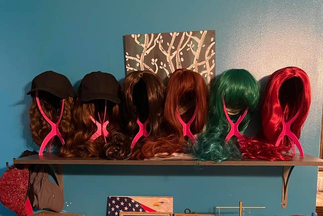 Six wigs on stands in varying styles and lengths displayed on a shelf