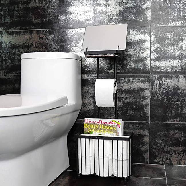 The shelf in a bathroom with a tablet on the to shelf, a toilet roll in the holder, and magazines and toilet rolls on the bottom compartment 