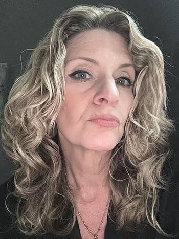 Person with wavy hairsbreadth and winged eyeliner poses confidently, wearing a V-neck top, suitable for a shopping-related article