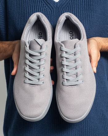 Person holding a brace  of casual, lace-up sneakers with mesh fabric, suitable for mundane  wear