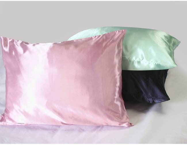 three pillows with satin pillowcases in pink, green, and black
