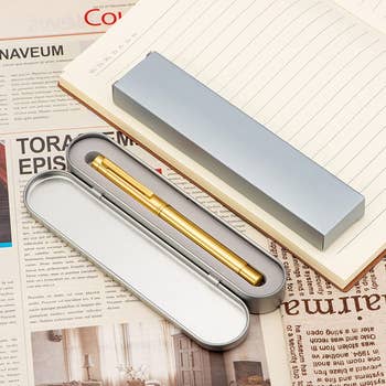 the gold pen in its storage case next to a notepad