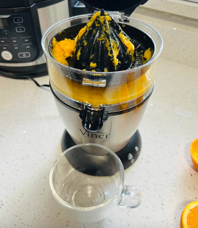 Electric citrus juicer connected  a room  countertop with caller  orangish  pulp and a solid  cupful  beneath   it