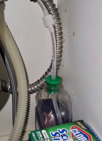 reviewer showing the soap bottle under their sink with the tube inside it which leads to the dispenser on top