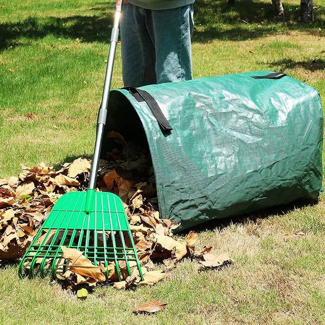 A person standing next to the dust pan with leaves and a rake nearby 