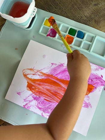 a reviewer's child using the painting station with a spot for paints and built in water cup