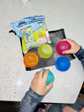 reviewer playing with the set of five different colored water balloons