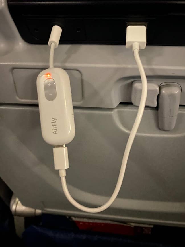 AirFly Bluetooth transmitter plugged into an airplane’s in-flight entertainment system with a white audio cable attached