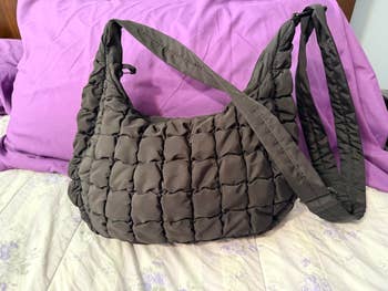 Quilted shoulder bag with a wide strap, perfect for everyday use, displayed on a bed with purple linens