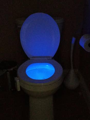 a reviewer photo of the light installed on the same toilet shining a blue light in the toilet bowl 