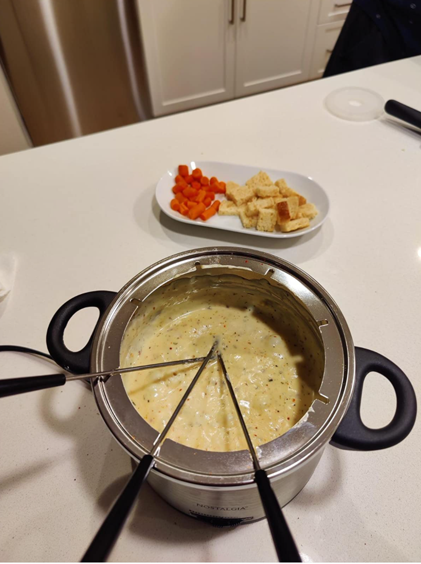 A small metal fondue pot with handles full of melted cheese and three sticks 