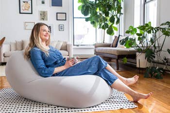 Model lounging reclined on a smooth gray bean bag chair on top of triangle patterned carpet