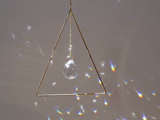a golden triangle with a crystal hanging in the center that reflects rainbows