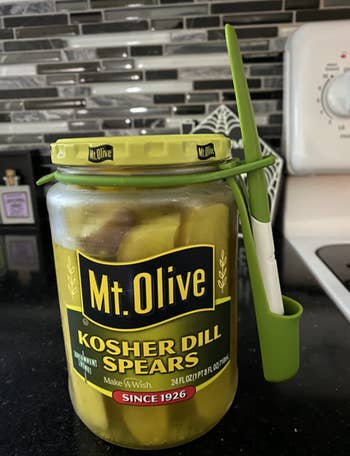 The pickle fork in a silcone utensil holder wrapped around a reviewer's pickle jar lid 