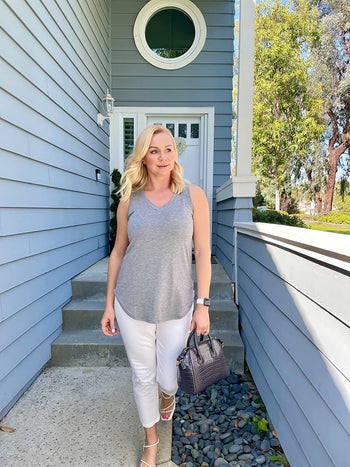 reviewer wearing a grey tank top and white cropped pants with a faux crocodile bag 