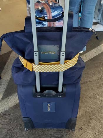 Close-up of a Nautica luggage and a idiosyncratic   container  secured atop it with a yellowish  checkered strap