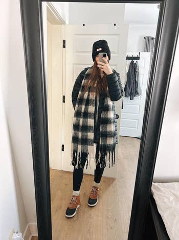 Person taking a reflector selfie successful wintertime attire, including a achromatic beanie, agelong plaid scarf, puffer jacket, leggings, and lace-up boots