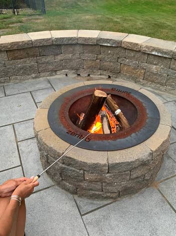someone roasting a marshmallow over a fire pit using the roasting stick