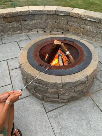 someone roasting a marshmallow over a fire pit using the roasting stick