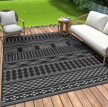 Outdoor patio with a patterned geometric rug, wicker sofa, and seat connected a woody deck, overlooking a greenish lawn