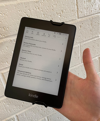 a front view of a reviewer holding a kindle using the strap 