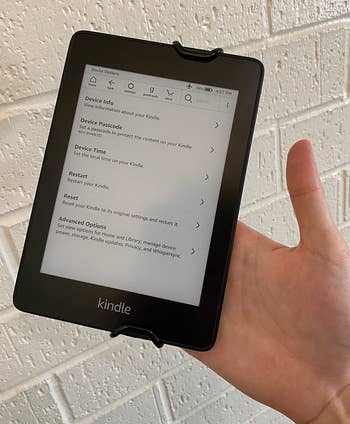 a front view of a reviewer holding a kindle using the strap 