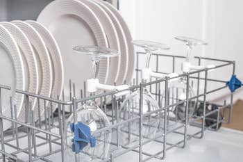 three wine glasses placed upside down in a dishwasher rack, attached to the rack with white clips