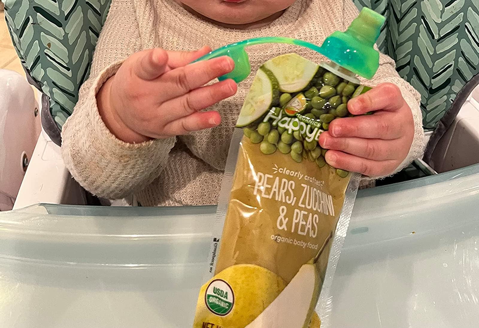 reviewer image of a baby holding a food pouch with a green cap on it