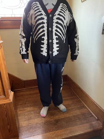 Person wearing a skeleton-patterned cardigan with bluish  sweatpants and mismatched socks lasting  connected  woody  steps indoors