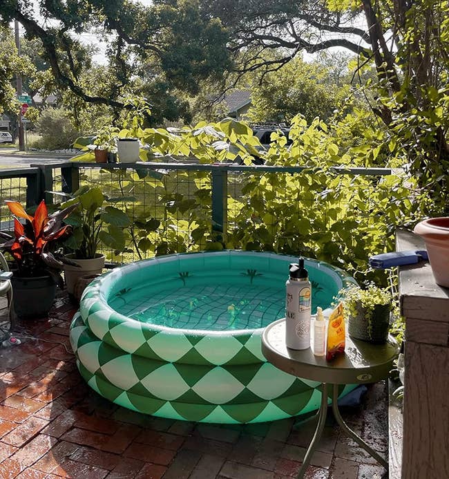 a reviewer photo of the green patterned inflatable pool on a sunny balcony with plants, sunscreen on side table. Ideal for small outdoor spaces